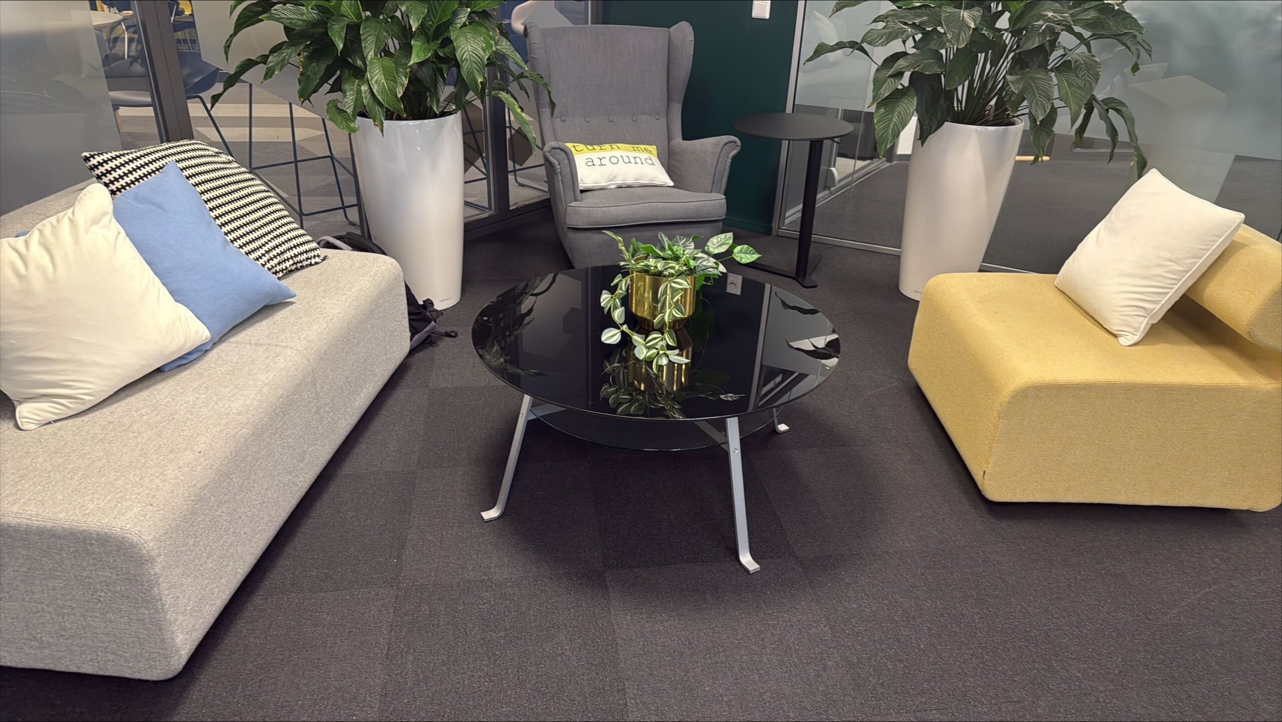 Kontorlounge med grå sofagrupper, gule pynteputer og planter